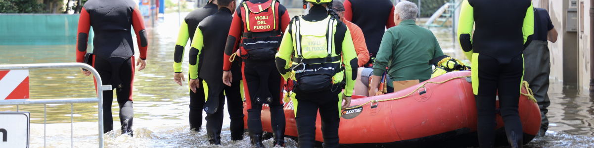Squadra di soccorritori in tute e giubbotti di salvataggio trascina un gommone rosso attraverso l'acqua alta durante un'alluvione