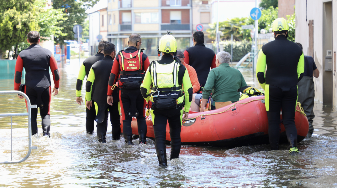 Soccorritori in tute da immersione e giubbotti di salvataggio trainano un gommone rosso attraverso una strada allagata in città durante un'alluvione