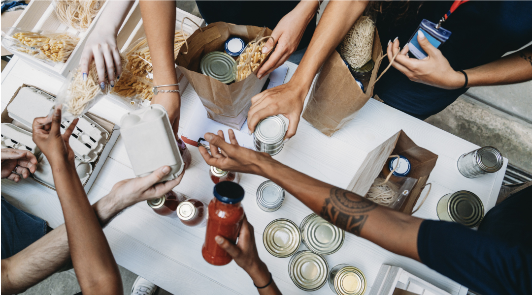 Vista dall'alto di volontari che preparano pacchi alimentari distribuendo vasetti, barattoli e generi alimentari in buste di carta