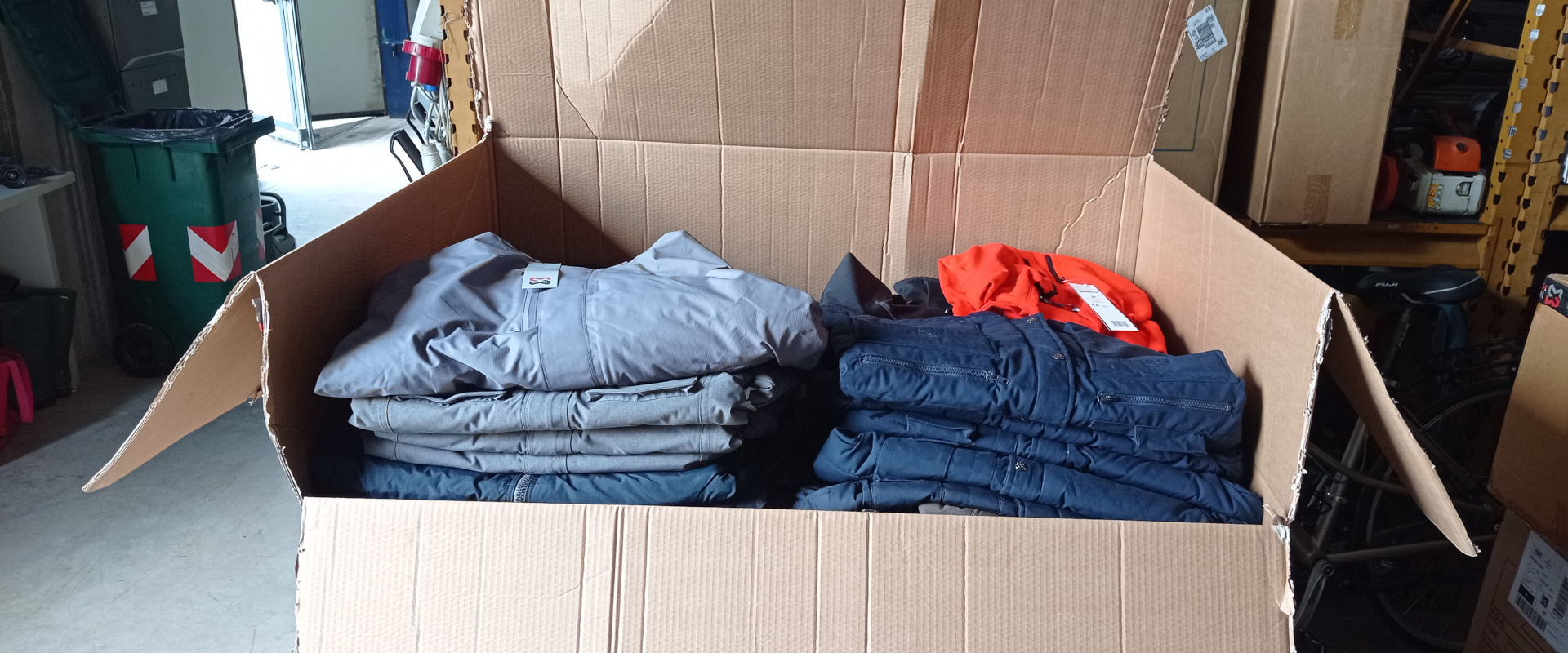 Grande scatola di cartone aperta contenente pile di abbigliamento da lavoro piegato in un magazzino, destinato alla donazione da parte di Würth MODYF