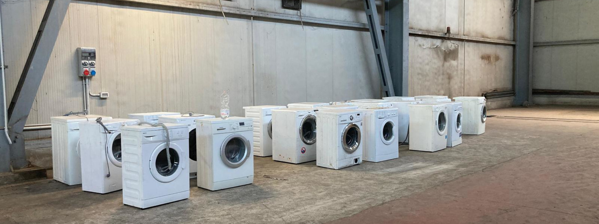 Fila di lavatrici bianche usate allineate in un magazzino, pronte per essere rigenerate e donate