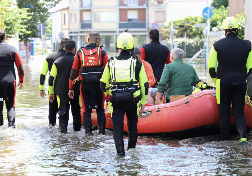 Squadra di soccorritori in tute e giubbotti di salvataggio trascina un gommone rosso attraverso l'acqua alta durante un'alluvione